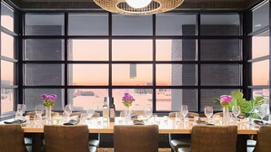 A dining table set for six with chairs, a vase with flowers, and a view of the cityscape through large windows.