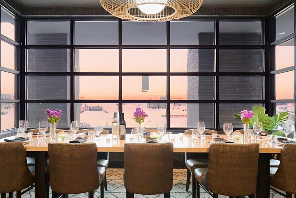 A dining table set for six with chairs, a vase with flowers, and a view of the cityscape through large windows. - Holiday Inn Hotel & Suites St. Catharines Conference Center by IHG (St. Catharines)