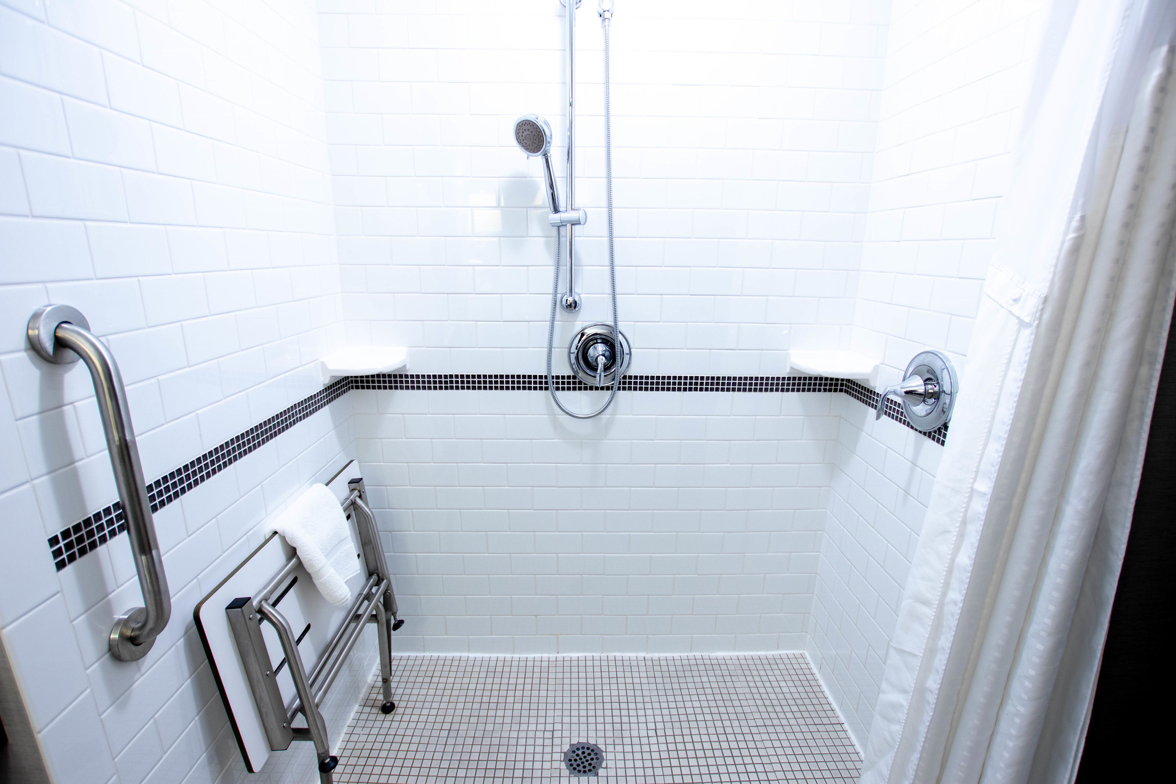 Ducha con azulejos blancos, cabezal de ducha manual y un soporte para toallas.