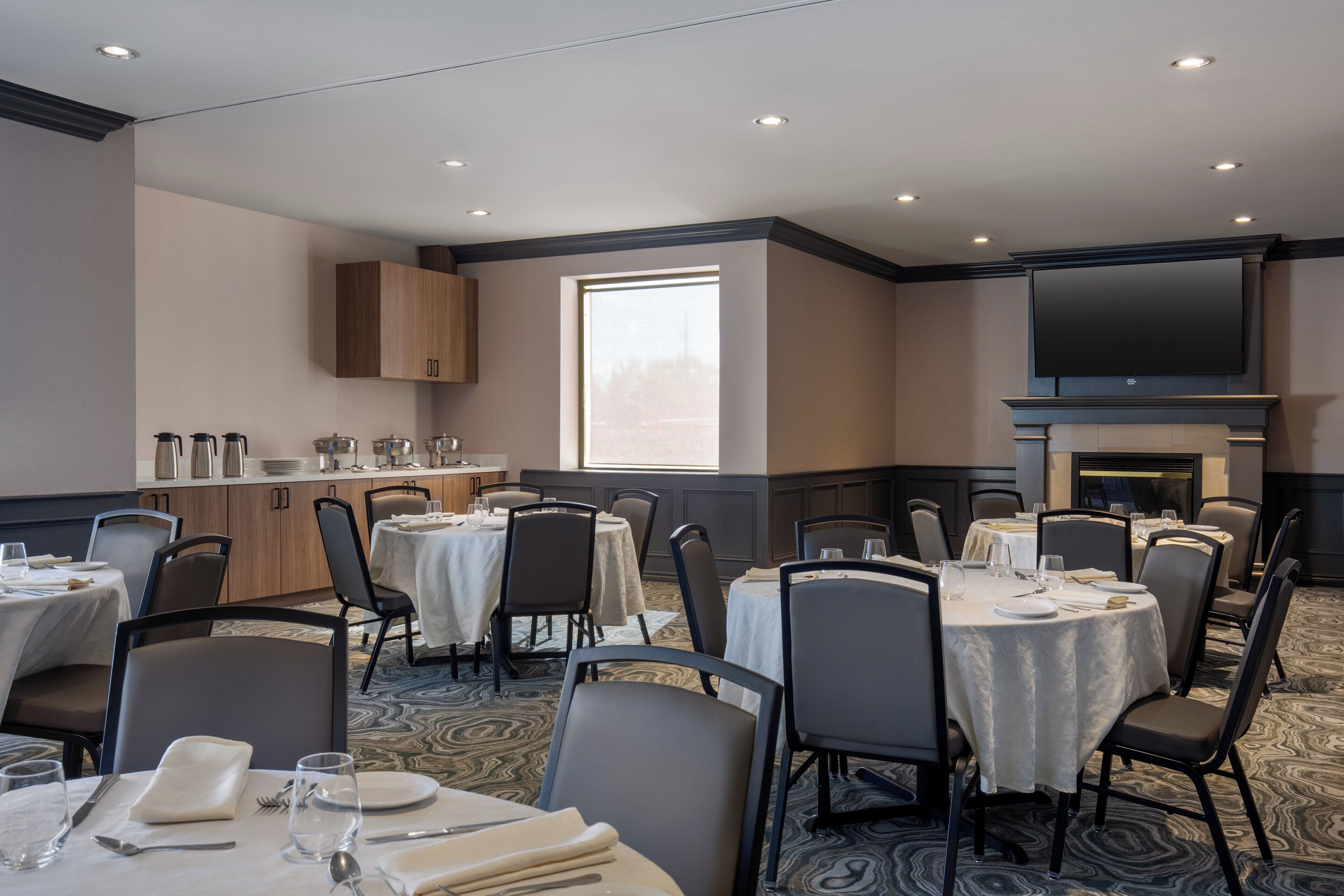 A conference room with round tables, chairs, a kitchen area, and a large TV screen.