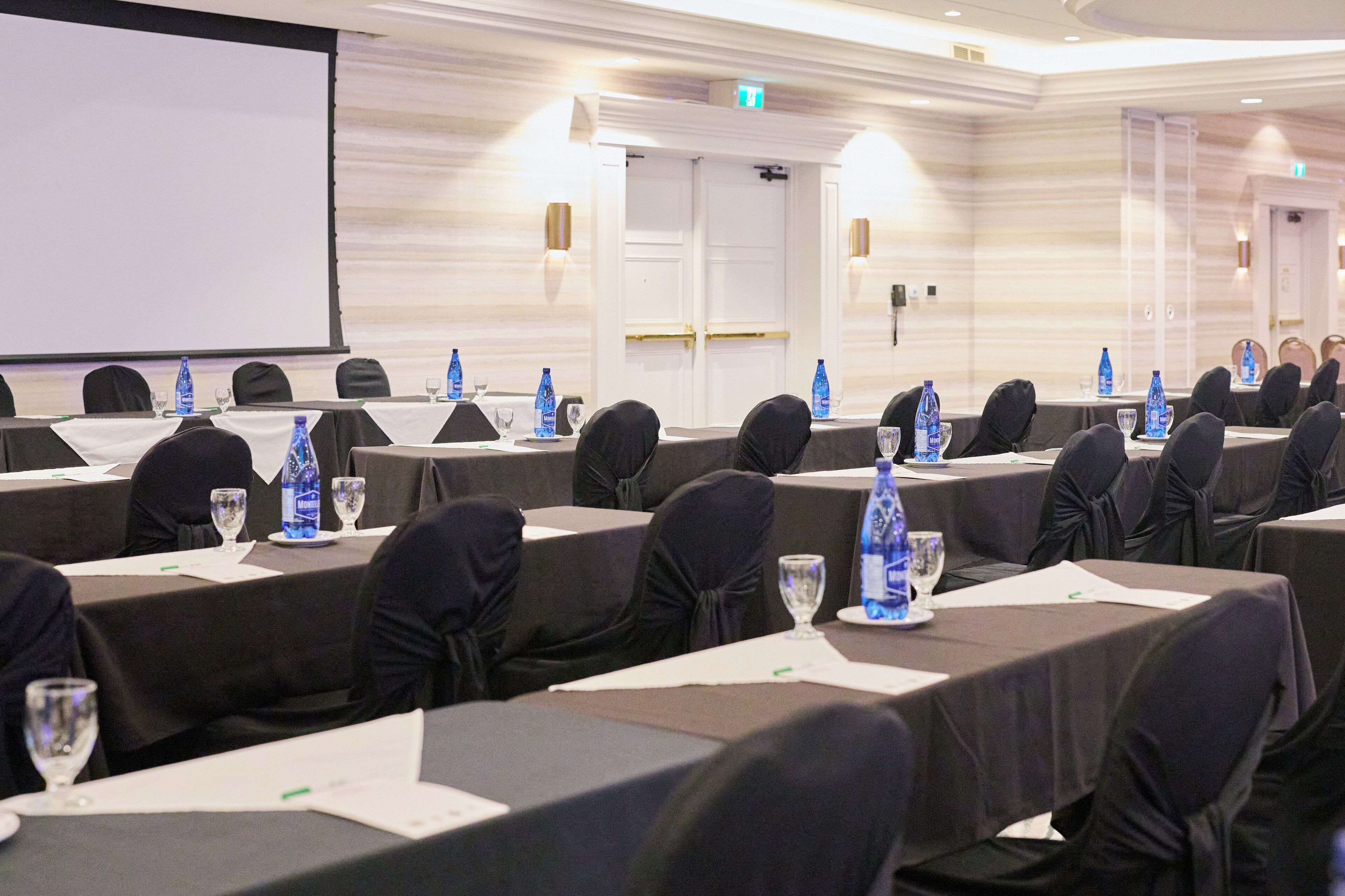 Un salón de conferencias con filas de mesas, cada una con una pantalla de proyector, botellas de agua y documentos.