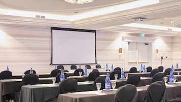 A conference room with tables set for a meeting, equipped with water bottles and glasses, in a room with a large screen and elegant ceiling design.