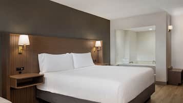 A modern hotel room with a large bed, wooden headboard, bedside lamps, a nightstand, and a bathroom visible through an open door.
