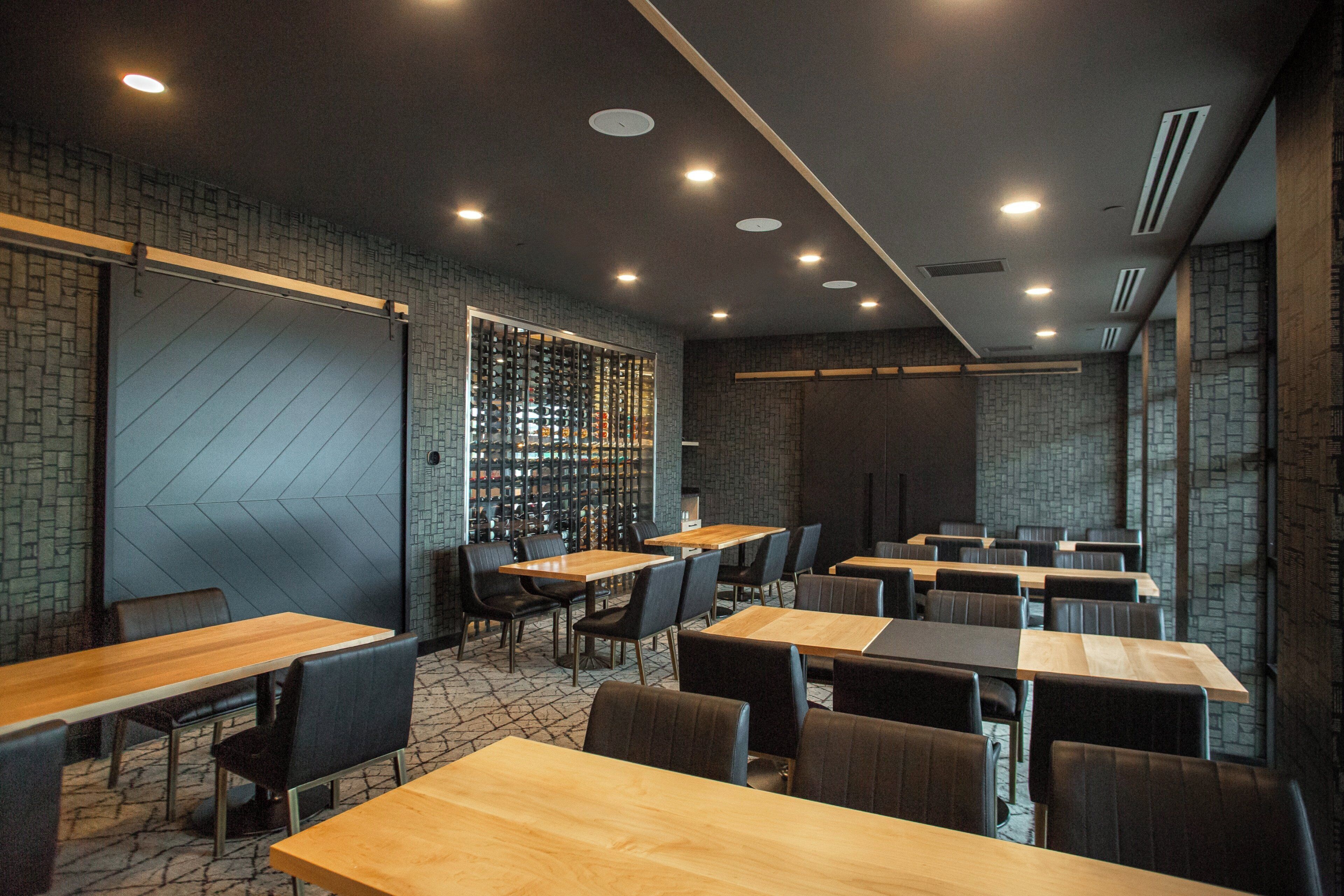 Un interior de restaurante moderno con paredes de ladrillo, mesas de madera y sillas negras.