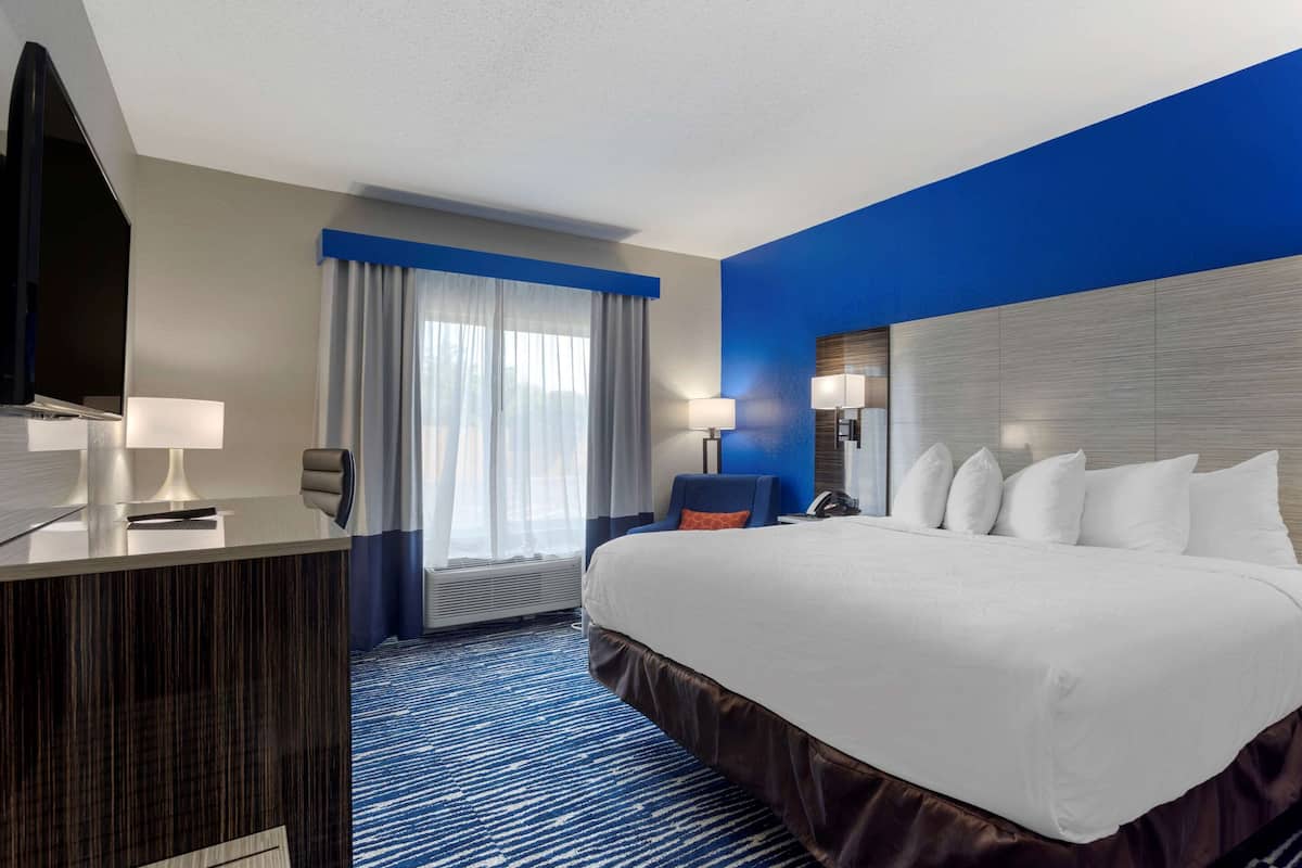 Habitación de hotel con una cama grande, un escritorio con silla, televisión y ventana con cortinas.
