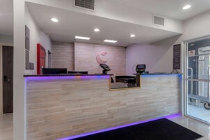 Un área de recepción con un mostrador de madera, una pantalla digital y una puerta de vidrio que da al exterior.