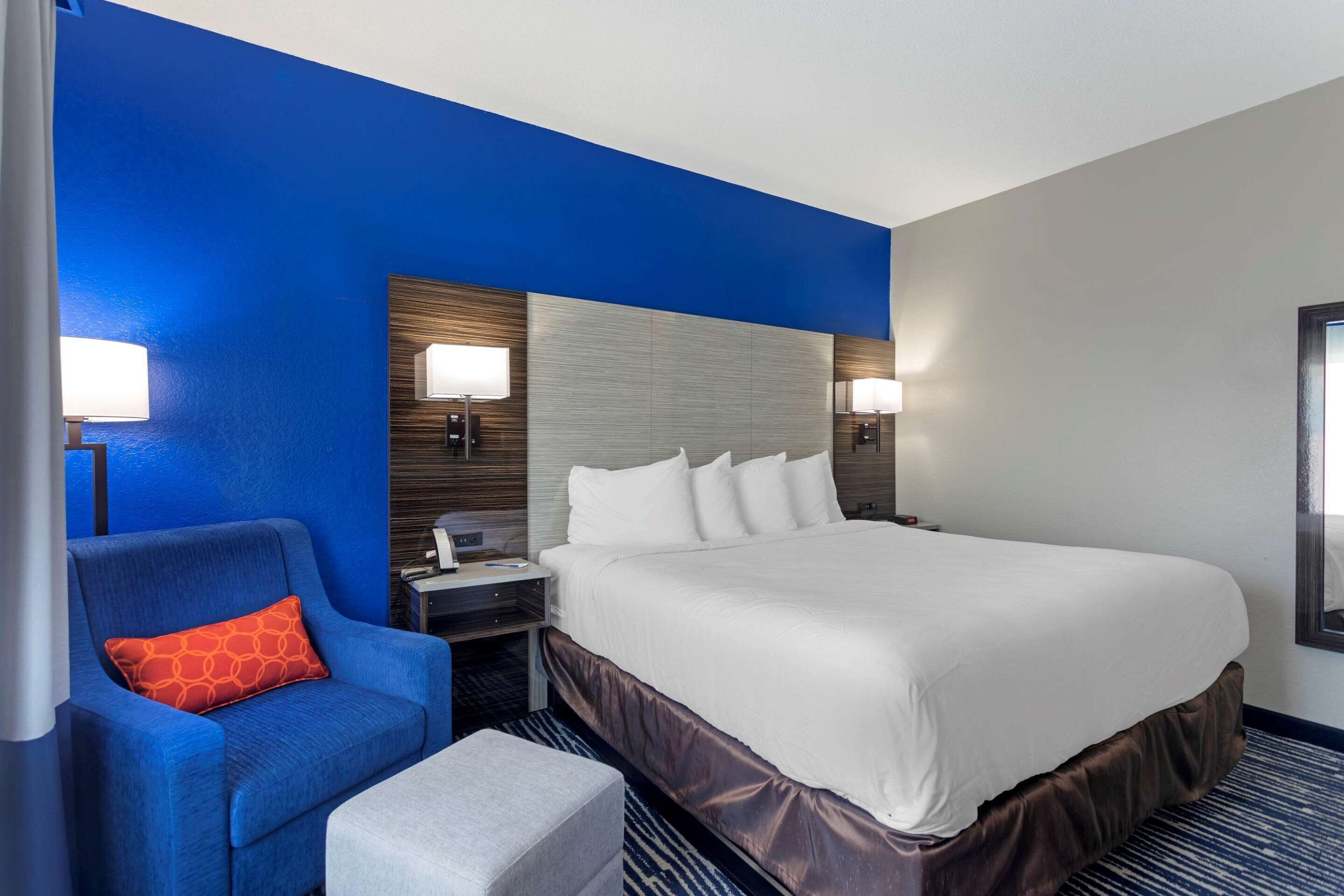 A hotel room with a large bed, a blue armchair, a nightstand, and two wall-mounted lamps.