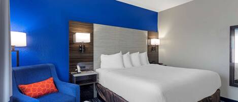 A hotel room with a large bed, a blue armchair, a nightstand, and two wall-mounted lamps.