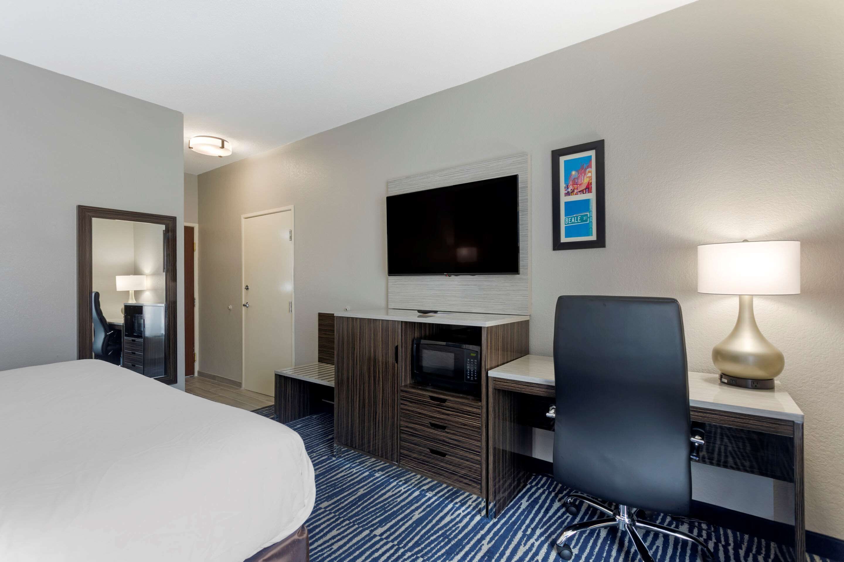 A hotel room with a bed, a desk with a computer, a TV, a lamp, and a mirror.