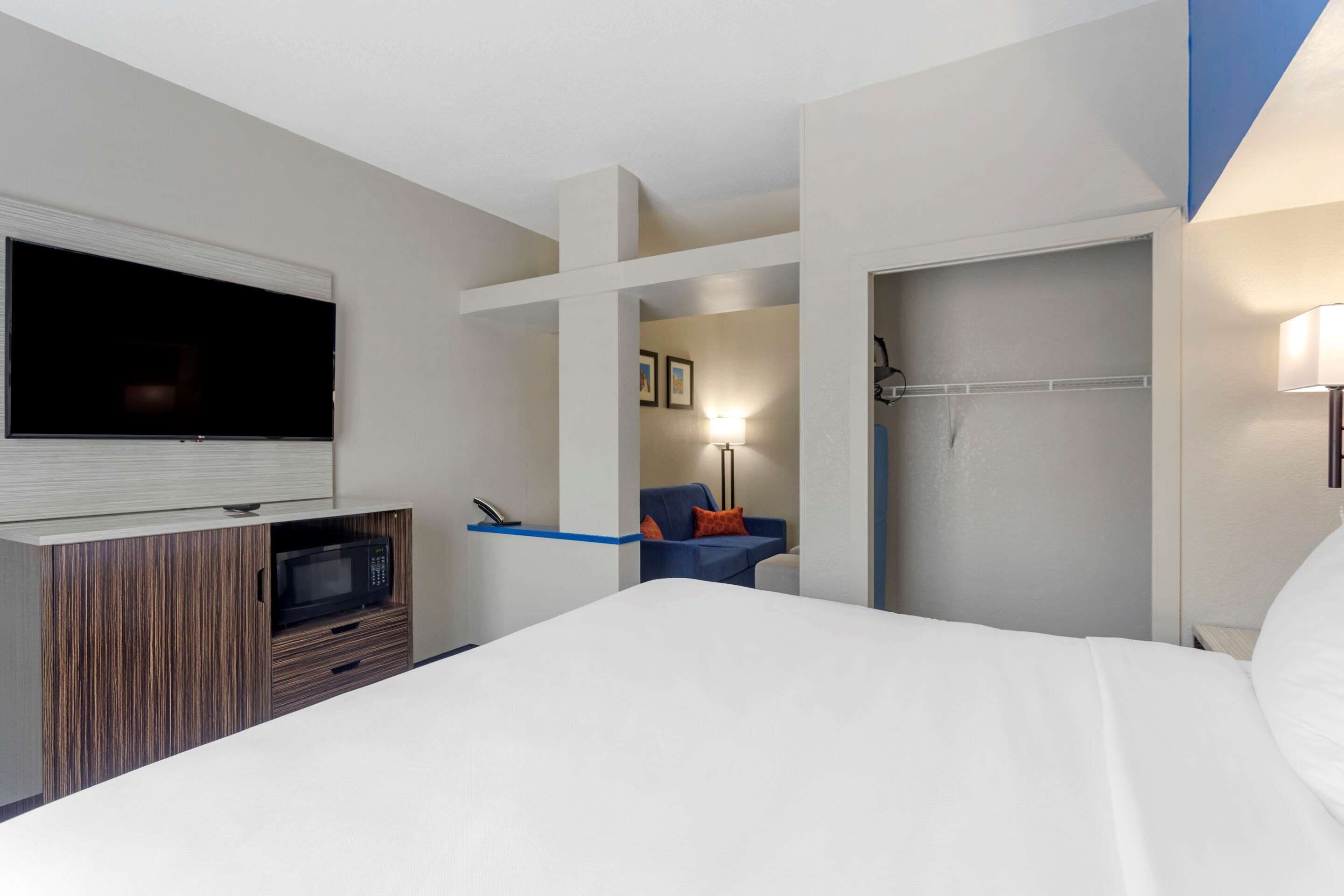 A hotel room with a bed, a TV, a microwave, a blue chair, and a door leading to a bathroom.