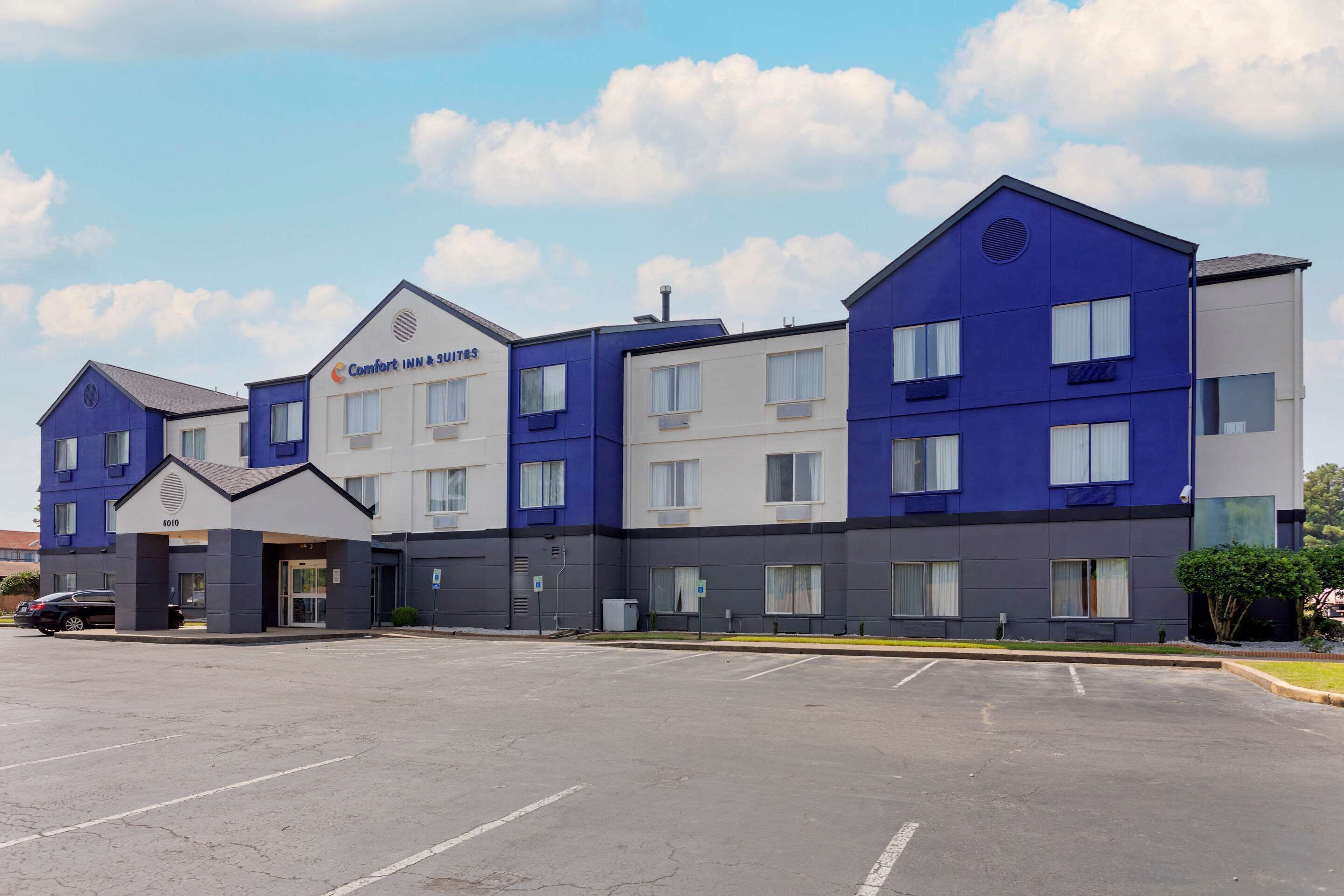 Um hotel de vários andares com design moderno, combinando cores azul e branco, e um estacionamento à frente.