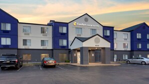 A hotel with a modern design, featuring a prominent 'Comfort Inn & Suites' sign. It has multiple floors with a mix of window styles and a parking lot with several cars. - Comfort Inn & Suites Memphis East (Memphis)
