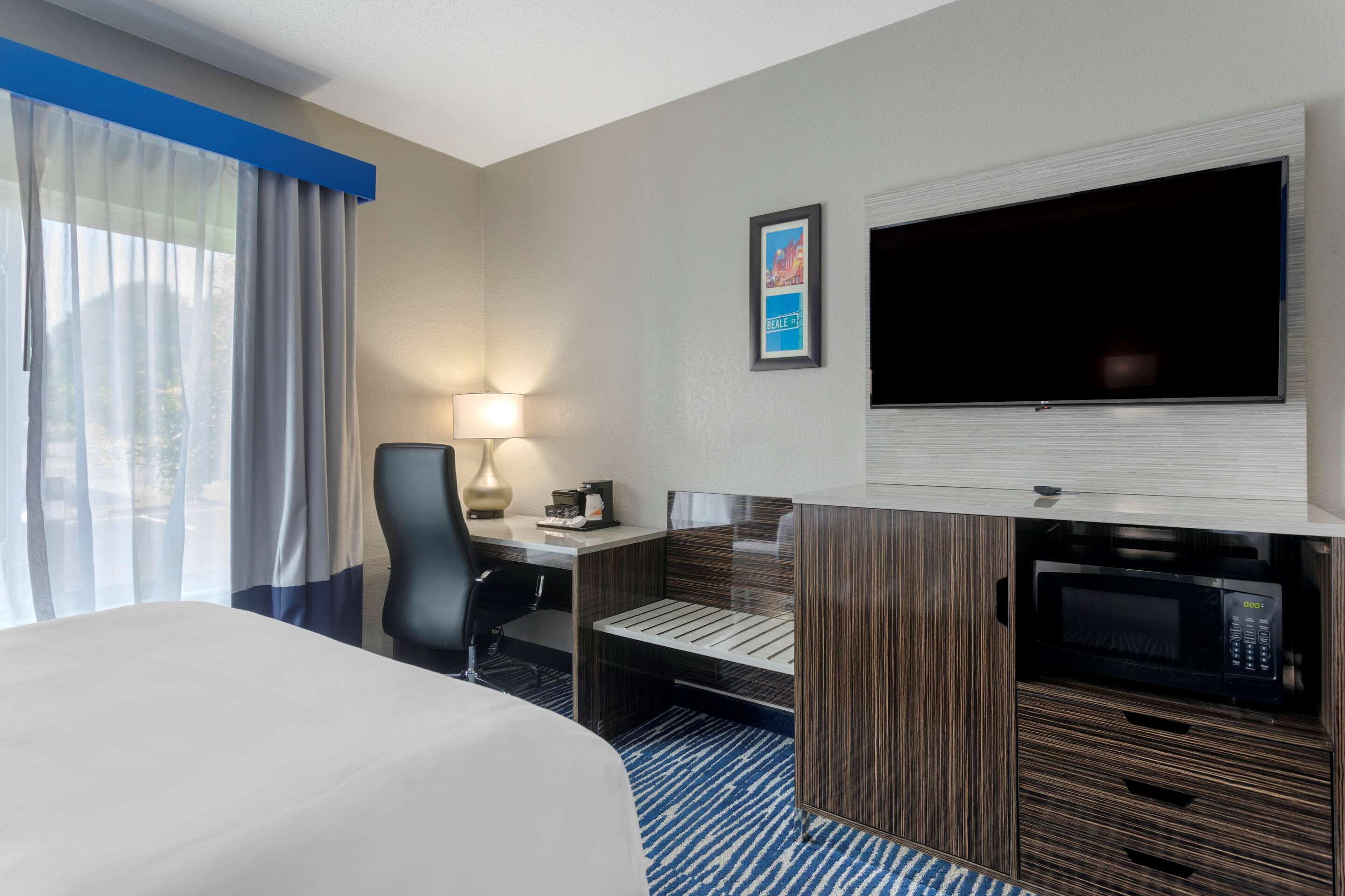 A hotel room with a bed, a desk with a lamp, a TV, and a microwave.