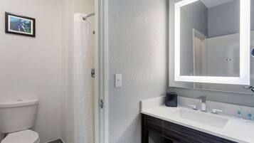 A bathroom with a toilet, shower, and sink with a mirror.