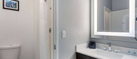 A bathroom with a toilet, shower, and sink with a mirror.