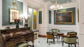 Een statige kamer met een groot schilderij, een antieke piano en stijlvol meubilair.
