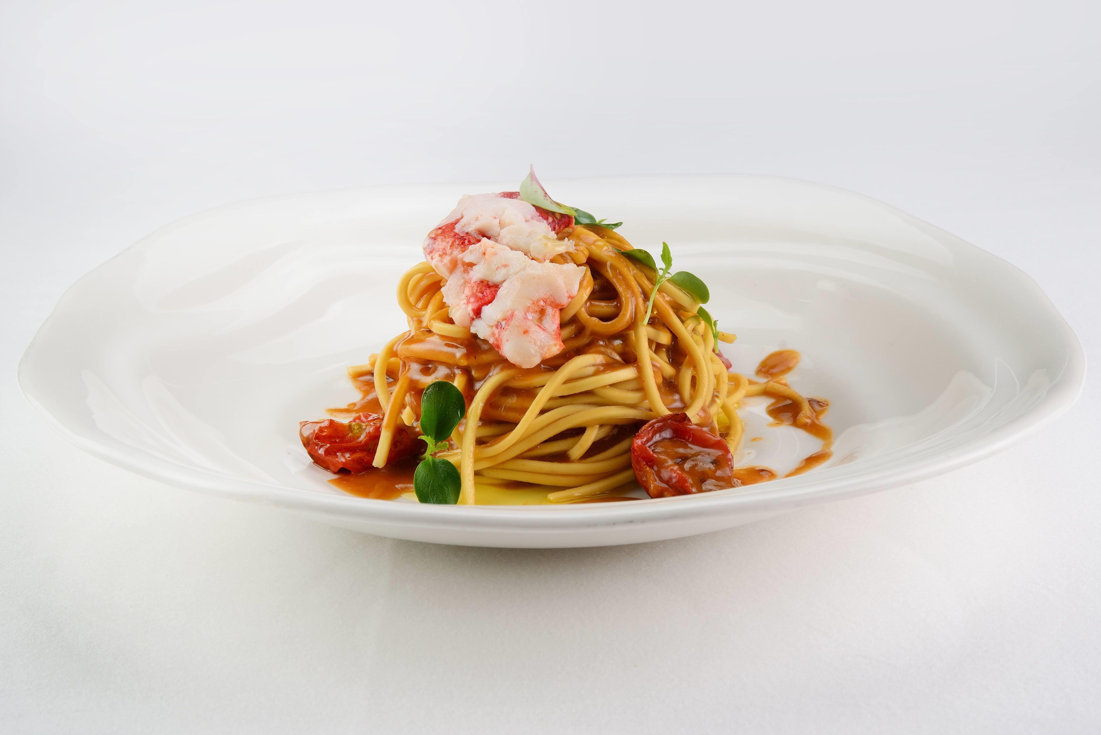 A plate of spaghetti with lobster, cherry tomatoes, and greens.