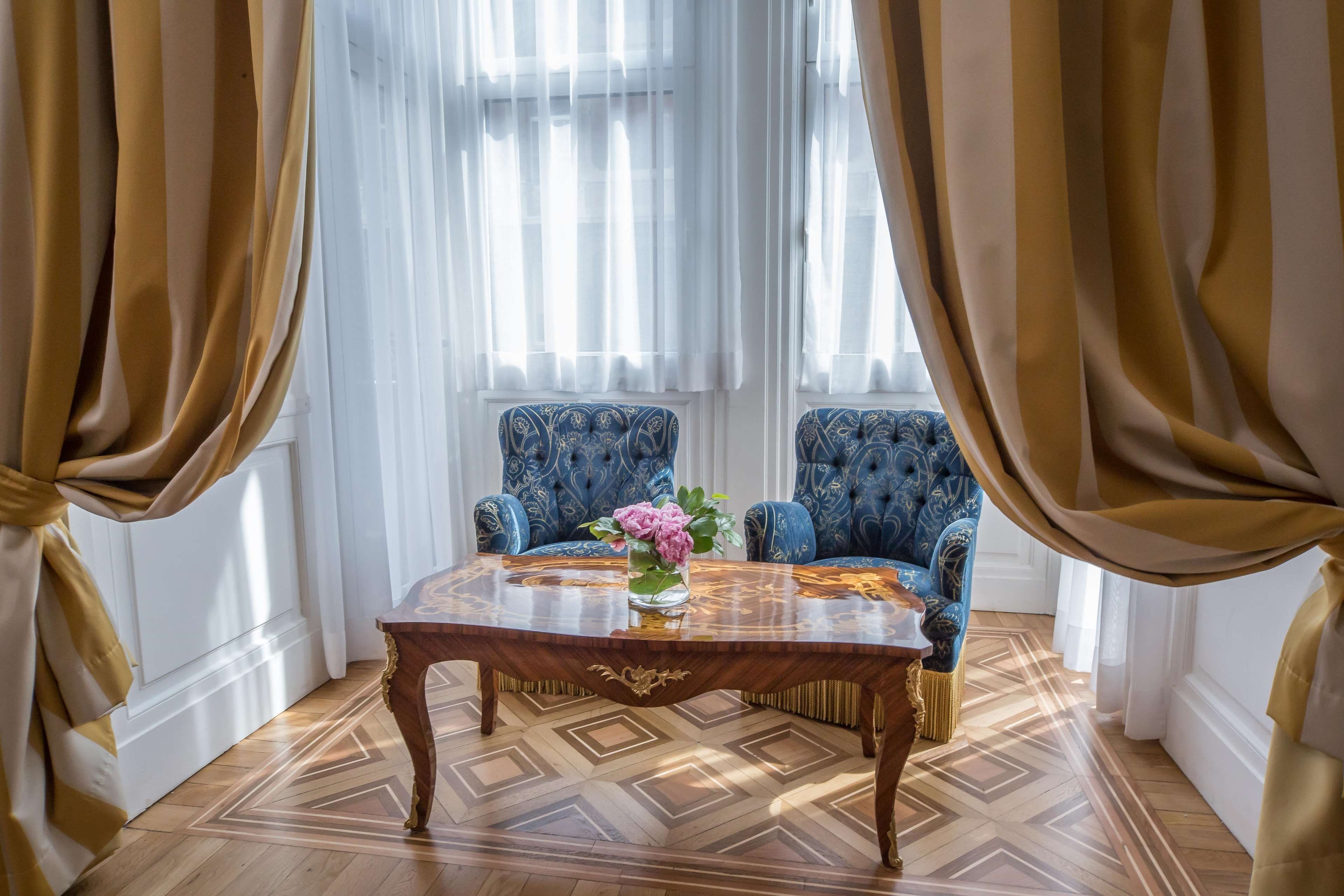 A room with two blue upholstered chairs, a wooden table with a vase of flowers, and a patterned floor.