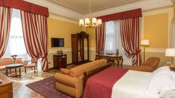 Une chambre d’hôtel avec un grand lit, deux fauteuils, un canapé, une table d’appoint en bois, un miroir et un lustre.