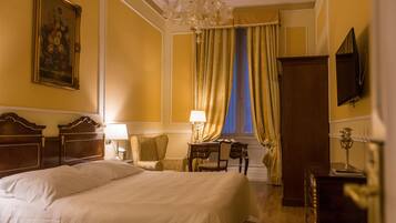 A hotel room with a large bed, a desk with a lamp, a chair, a television, and a window with curtains.