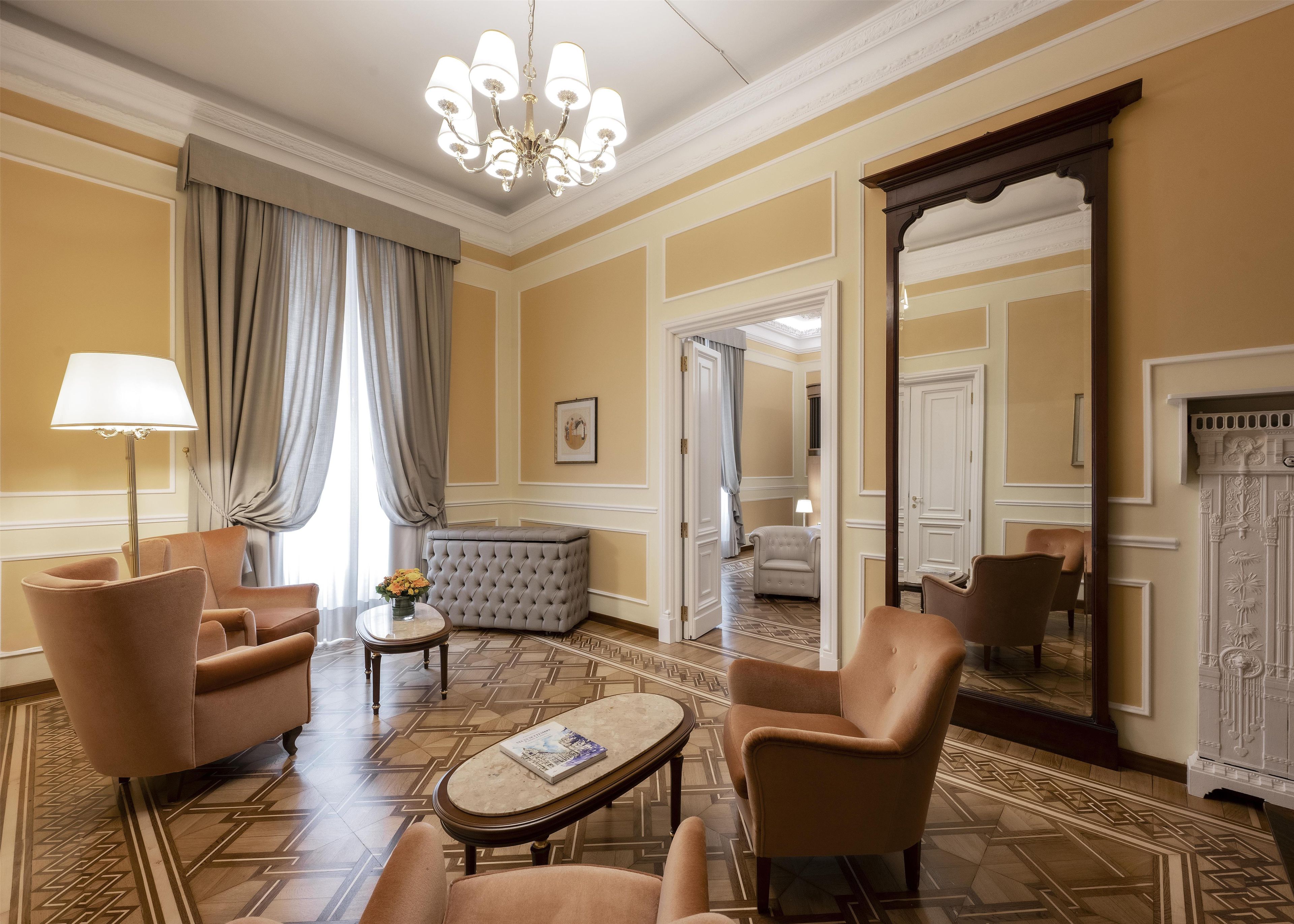 Een hotelkamer met een kroonluchter, comfortabele fauteuils, een klein rond tafeltje en een grote spiegel.