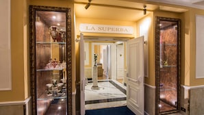 Un pasillo con piso de mármol, un expositor de vidrio con objetos decorativos y un cartel que dice "LA SUPERBA".