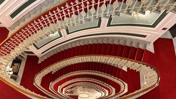 Un magnifique escalier, agrémenté de rampes décoratives et recouvert d’un tapis rouge, mène à un auditorium circulaire.