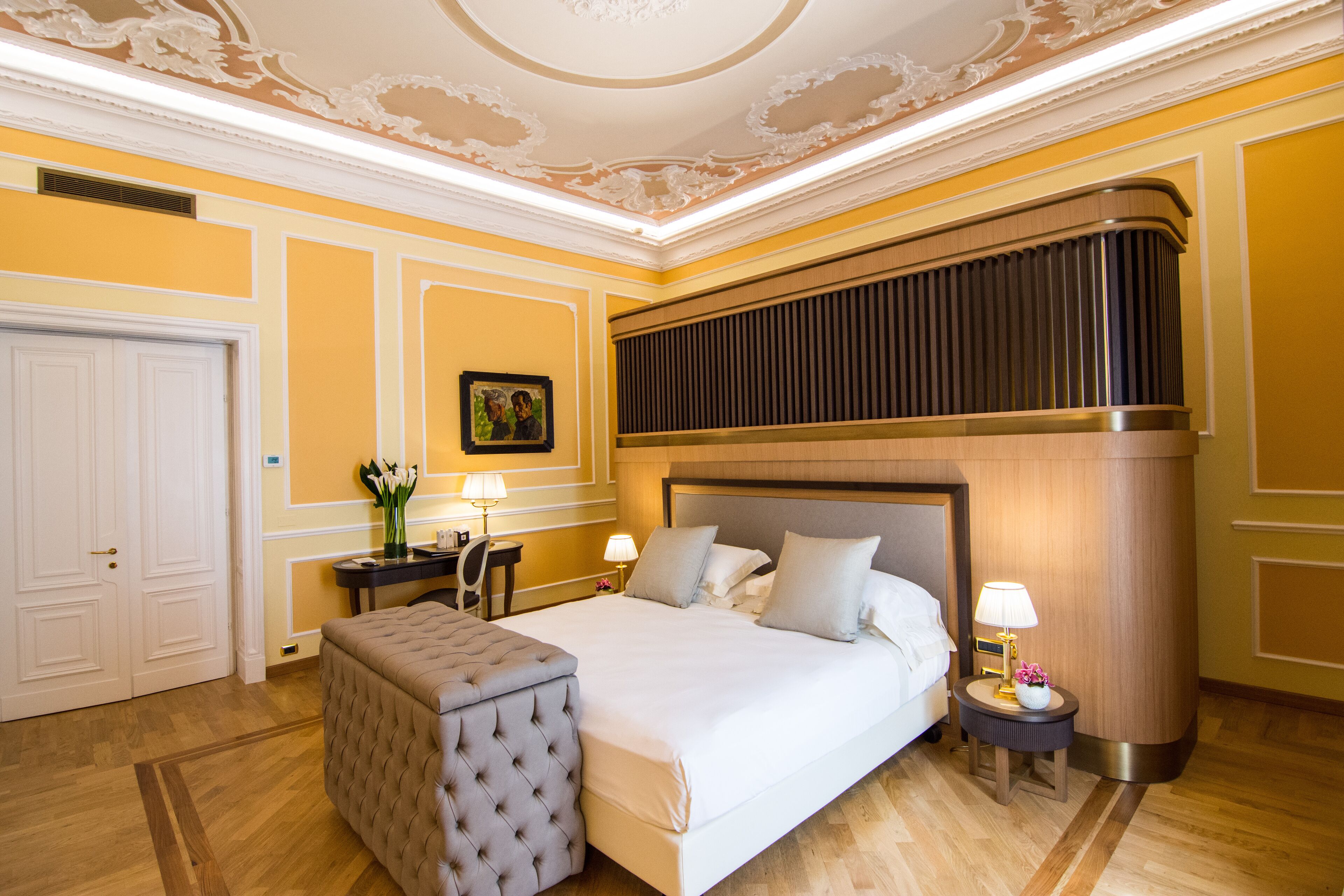 Een hotelkamer met een groot bed, een zithoek, een bureau en een decoratief plafond.