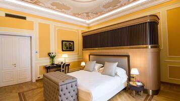 Een hotelkamer met een groot bed, een zithoek, een bureau en een decoratief plafond.