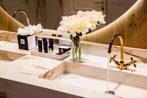 Un tocador de baño con encimera de mármol, grifo dorado y un espejo que refleja el tocador.