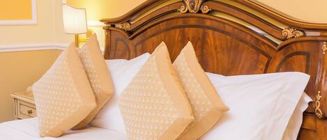 A bed with four patterned pillows, a wooden headboard, a bedside table with a lamp, and a framed picture on the wall.