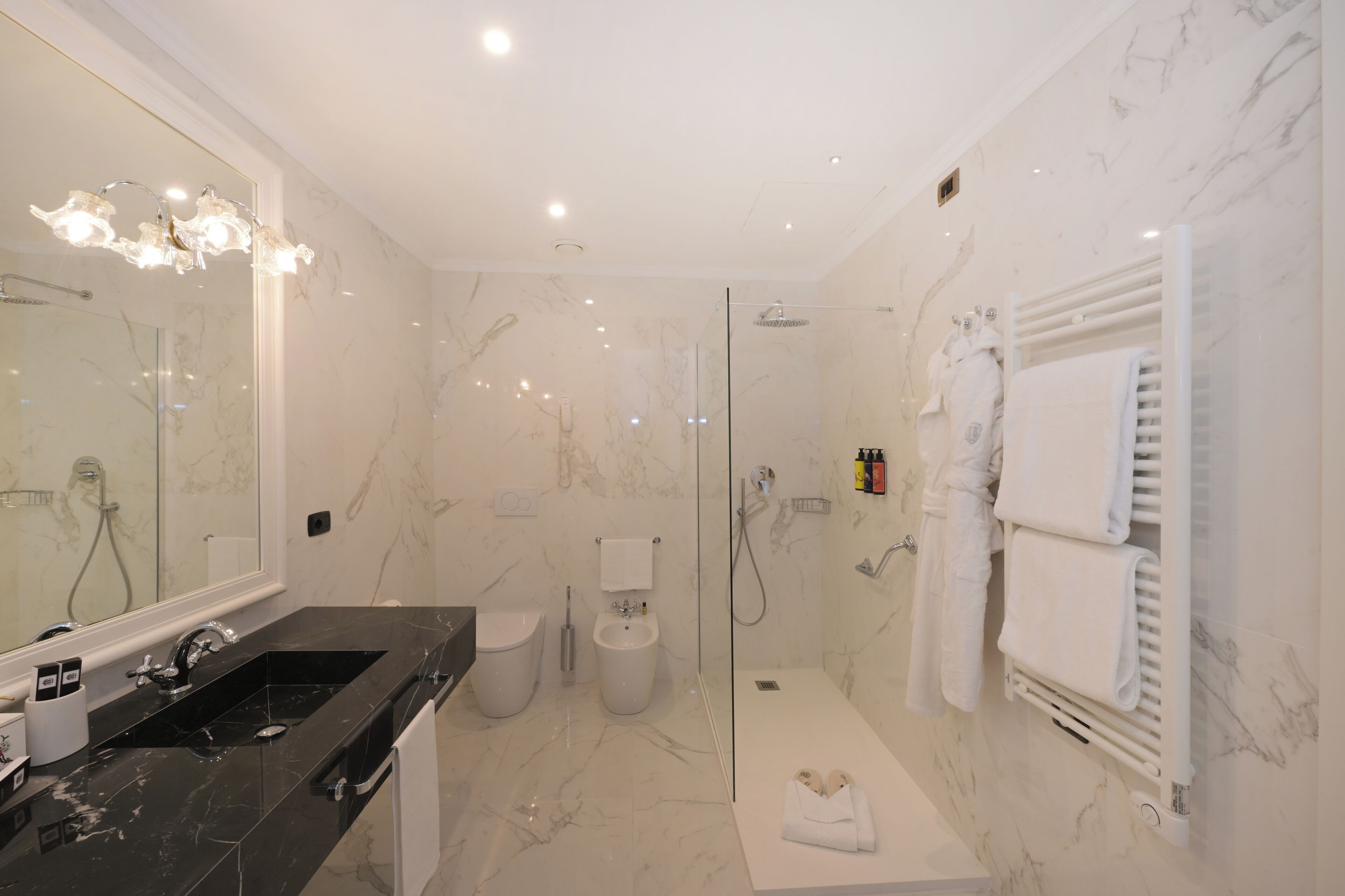 A modern bathroom with a marble floor, a glass-enclosed shower, a black sink, and a white towel rack.