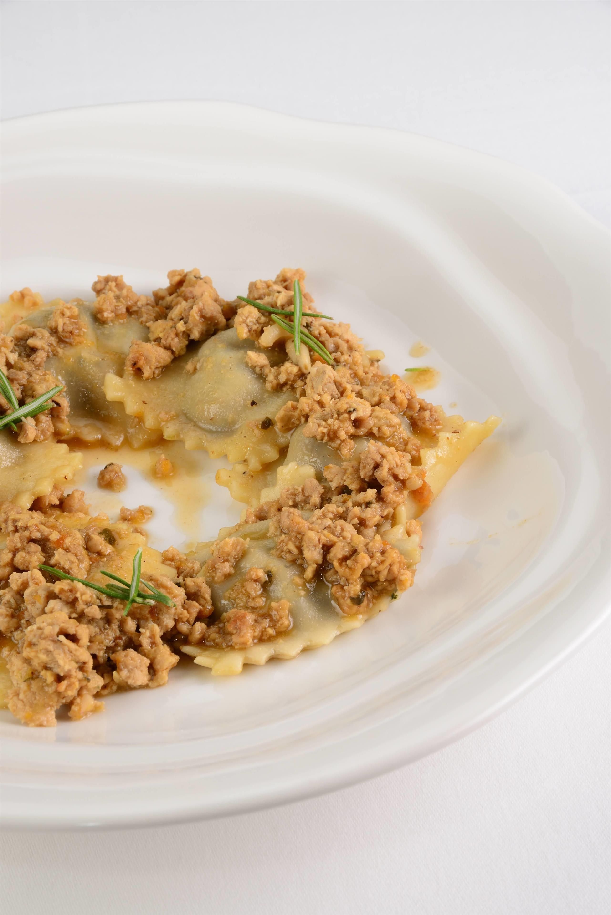 Un plato blanco con un guiso, posiblemente un tipo de albóndiga o pasta rellena, adornado con hierbas verdes.