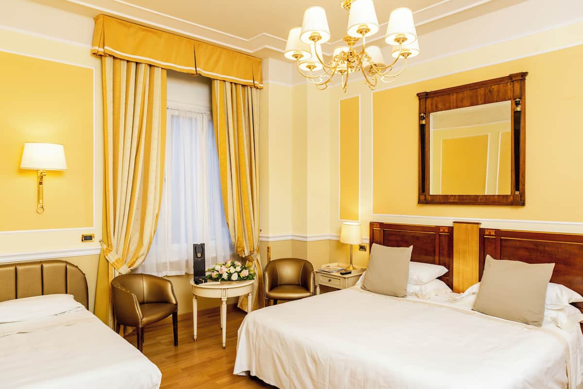 A hotel room with two beds, a sitting area with a table and chairs, a chandelier, and a large mirror on the wall.