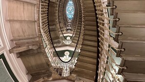 Una imponente escalera con barandilla ornamentada y un ventanal central de vitral.