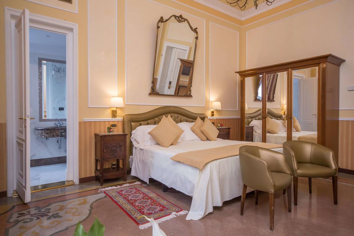 A hotel room with a bed, two bedside tables, a mirror, a chair, and a red patterned rug.
