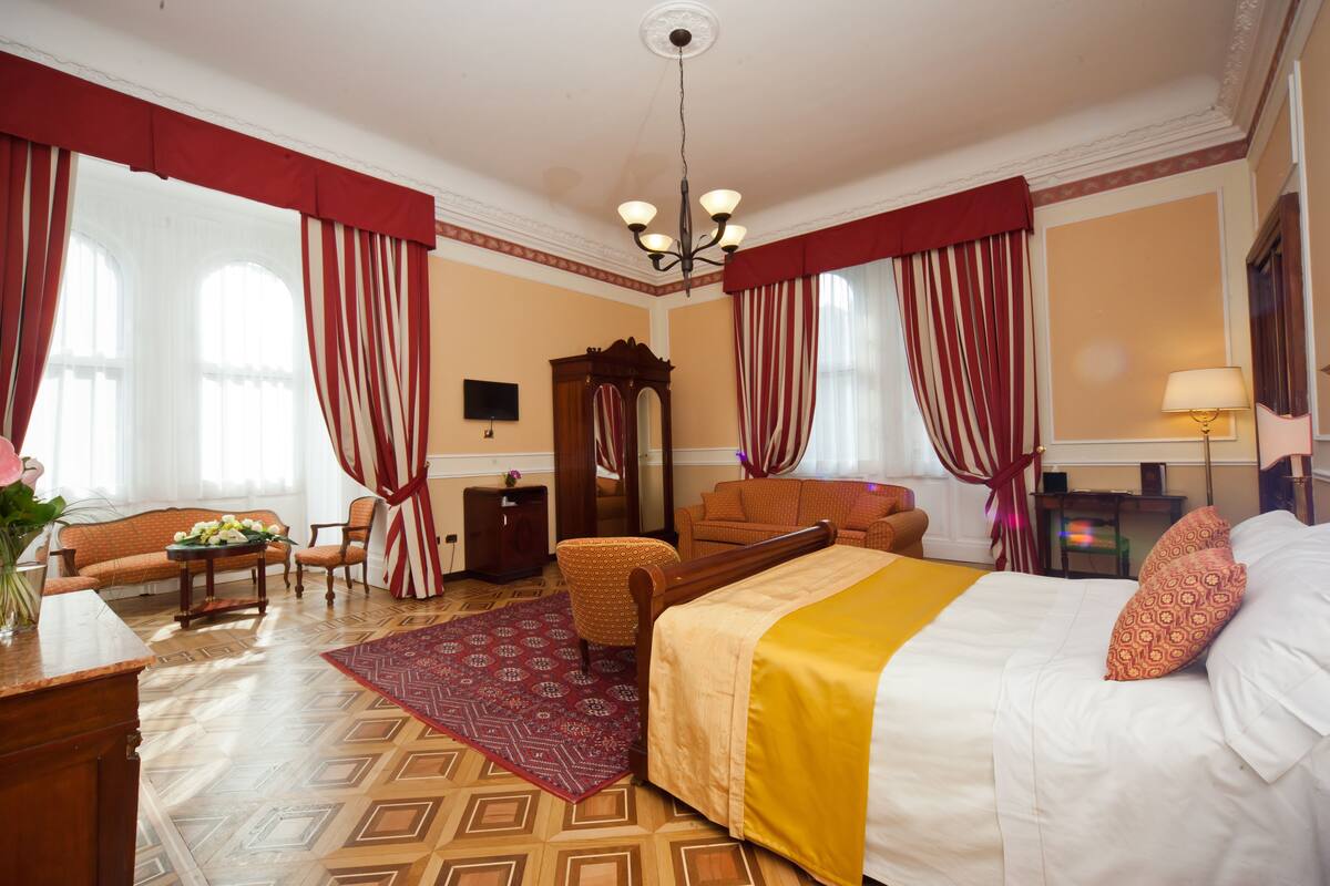 A hotel room with a bed, a sofa, a chair, a desk, and a mirror.