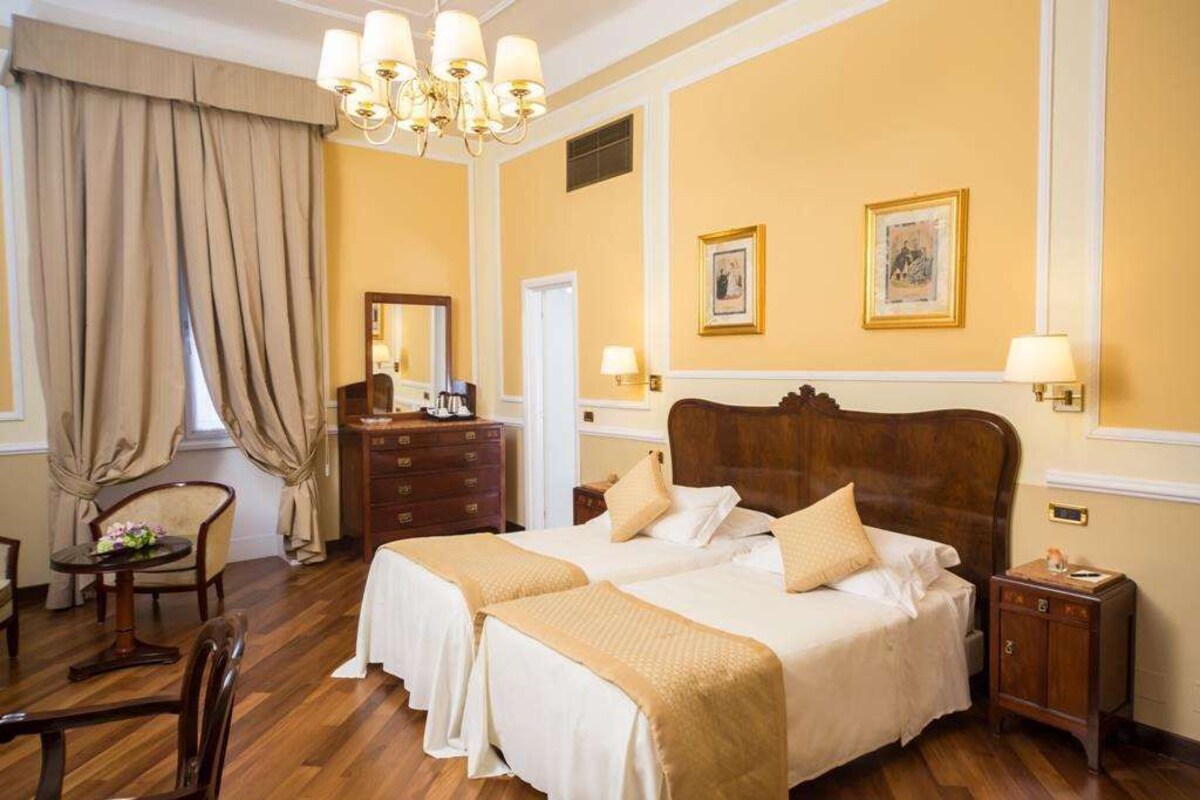 Habitación de hotel con dos camas, una araña, un aparador y un escritorio con una silla.