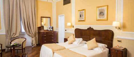 A hotel room with two beds, a chandelier, a dresser, and a desk with a chair.