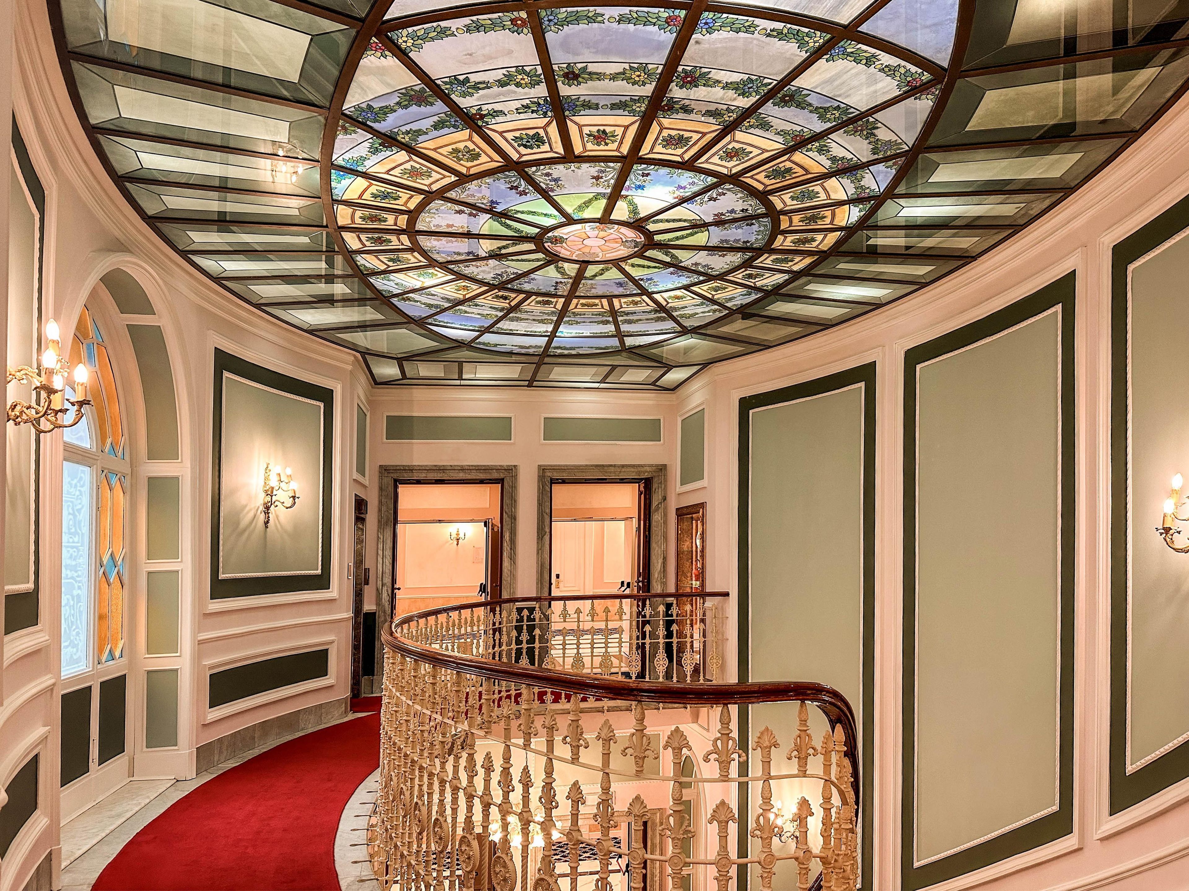 A grand hallway with a glass dome ceiling, a red carpet, and ornate railings.