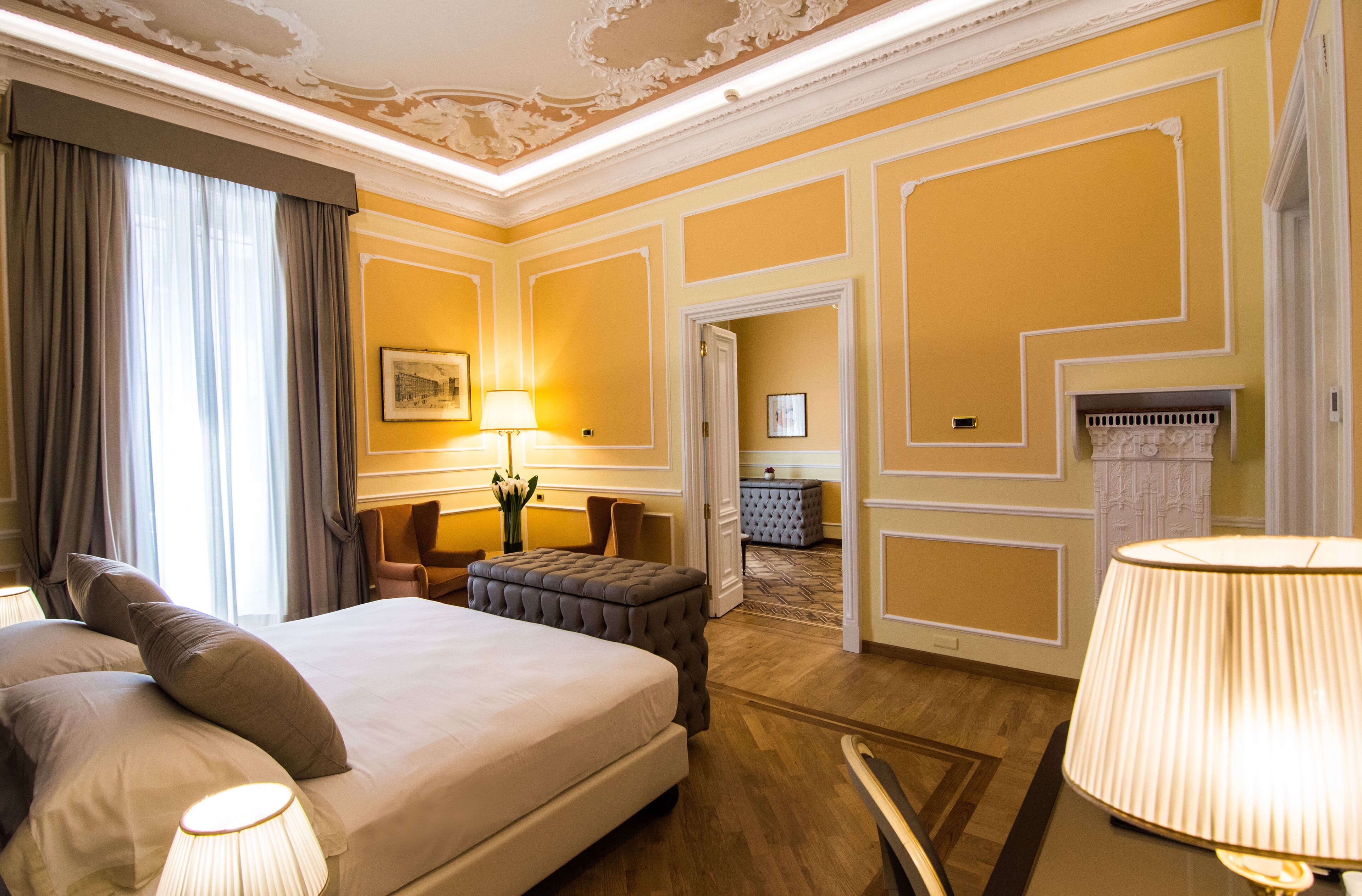 Una camera d'albergo con un letto grande, un'area salotto con una poltrona e poggiapiedi, una lampada e un caminetto.