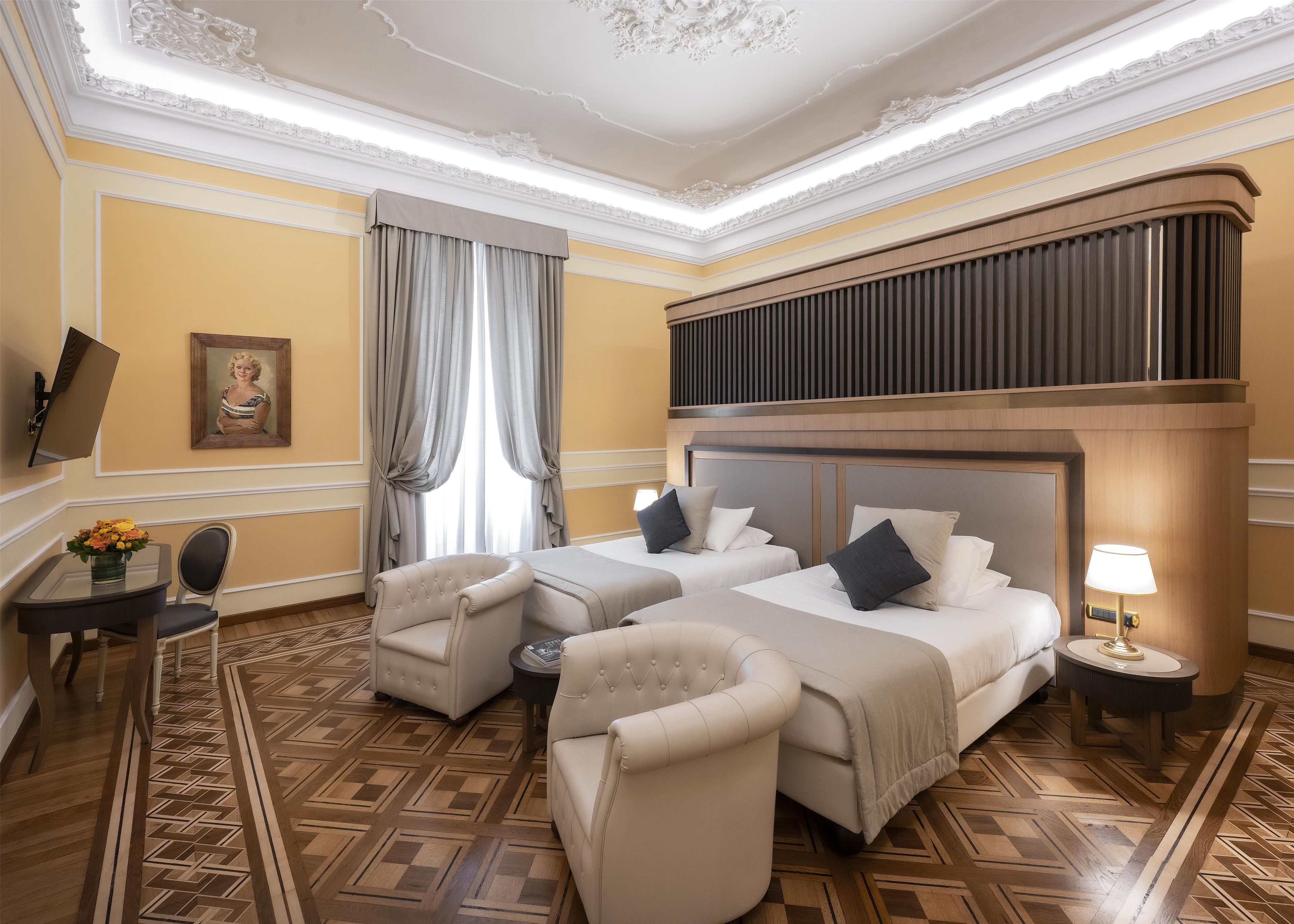 A hotel room with two beds, a sitting area with a chair, a small table, and a TV mounted on the wall.