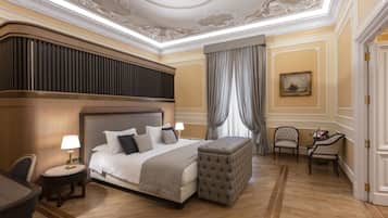 Habitación de hotel con una cama grande, una zona de estar con una silla, una mesita pequeña y un techo decorativo.