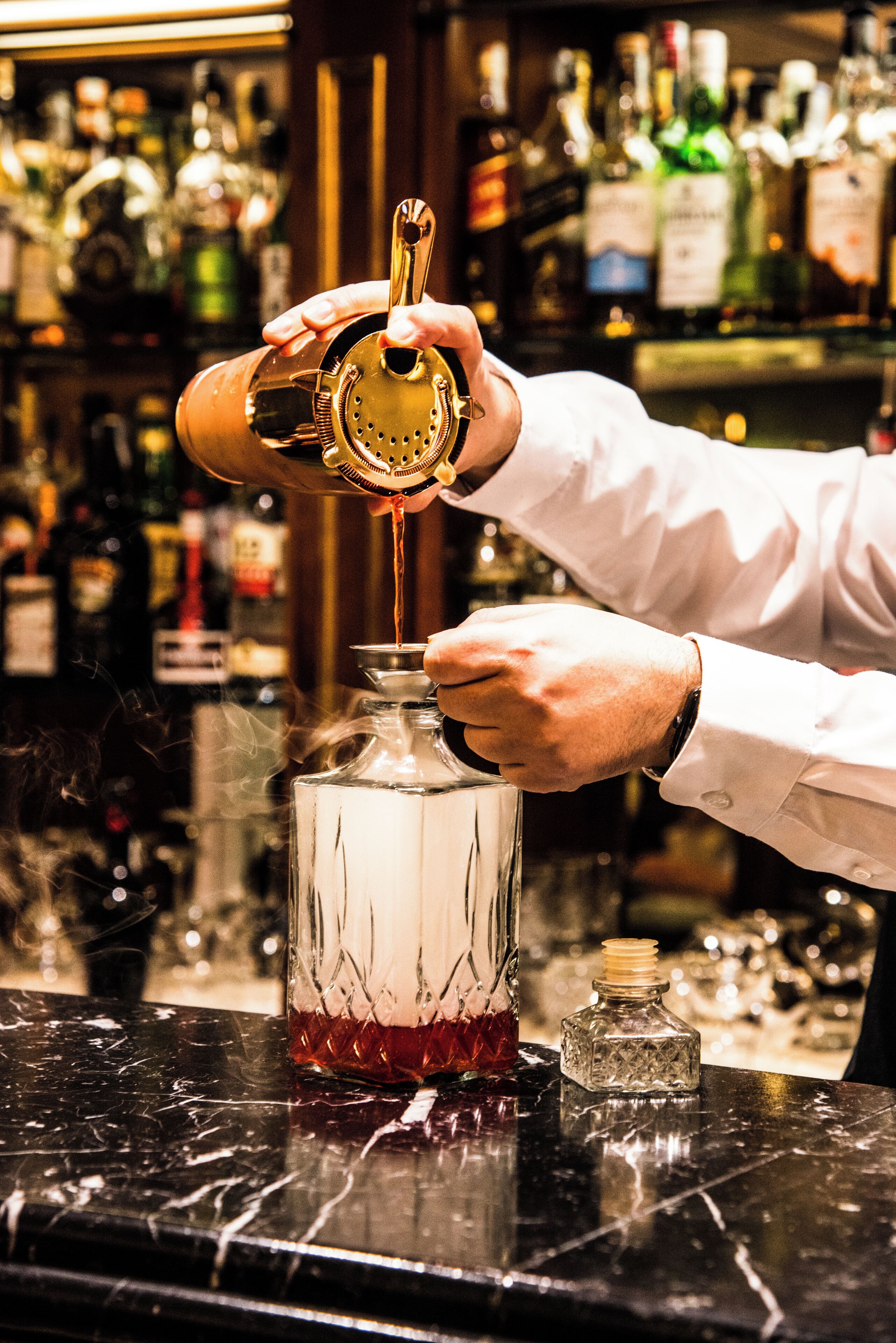 Un barman vertiendo una bebida en un vaso usando un dosificador.