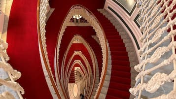 Una gran escalera ornamentada con alfombra roja y barandillas blancas con detalles intrincados, que conduce a un interior lujoso.