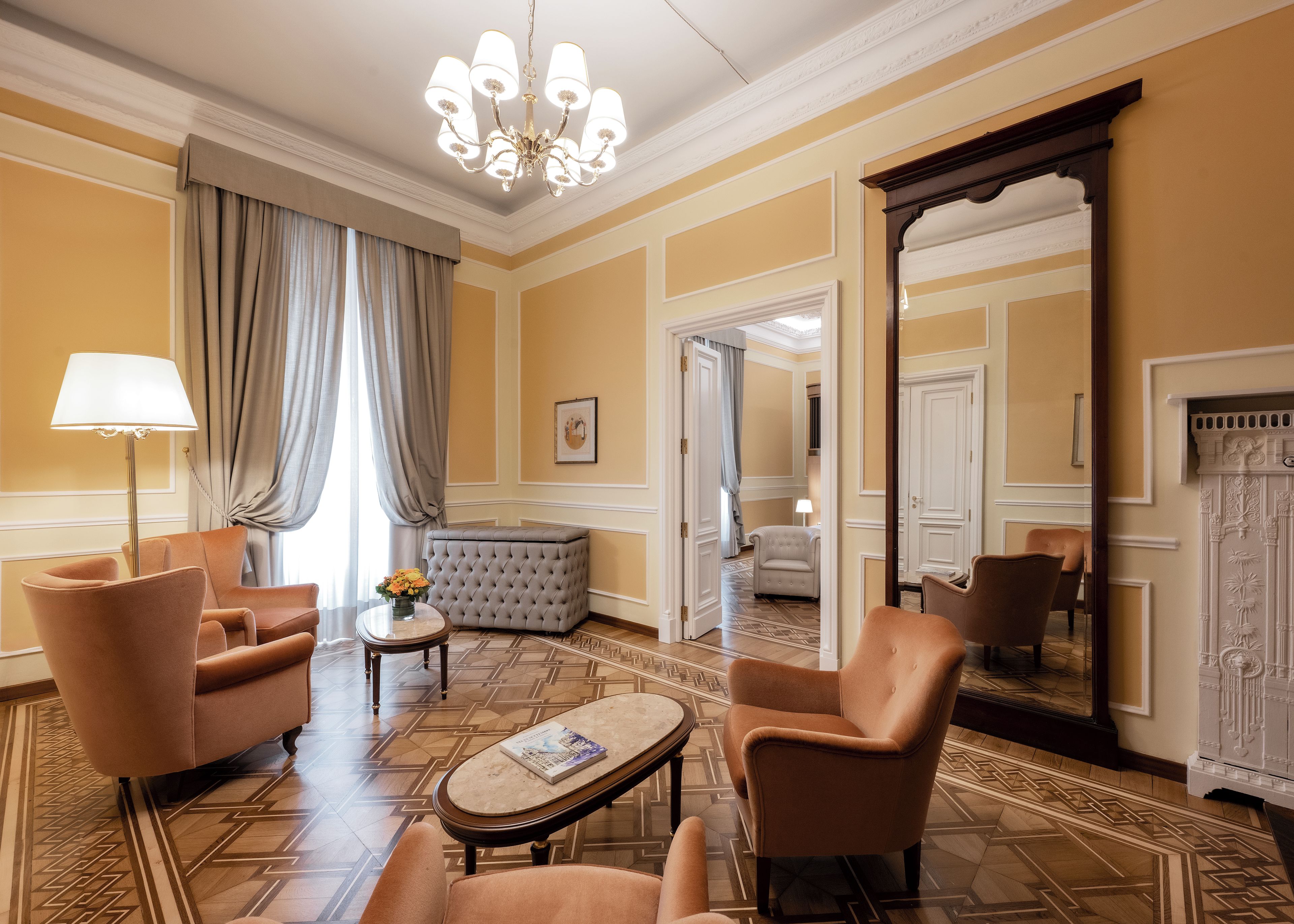 A room with a chandelier, two armchairs, a sofa, a small table with a book, and a mirror.