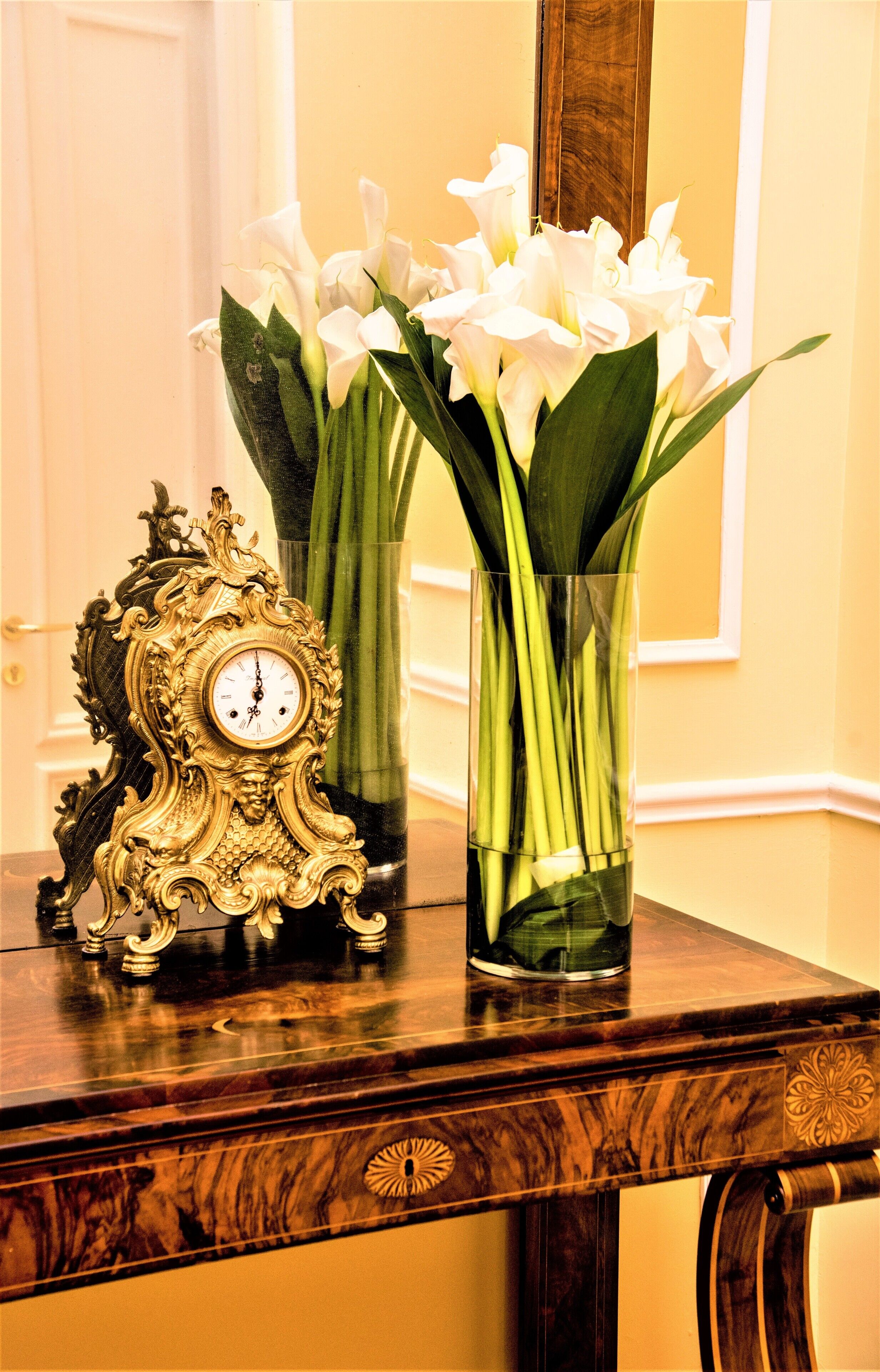 A wooden table with a decorative clock and two vases of white flowers.