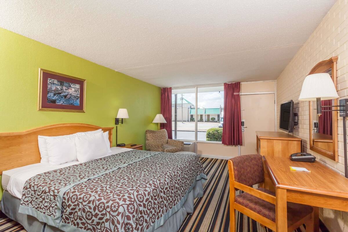 Une chambre d’hôtel avec un lit, un bureau, une chaise, une télévision et une fenêtre avec des rideaux.