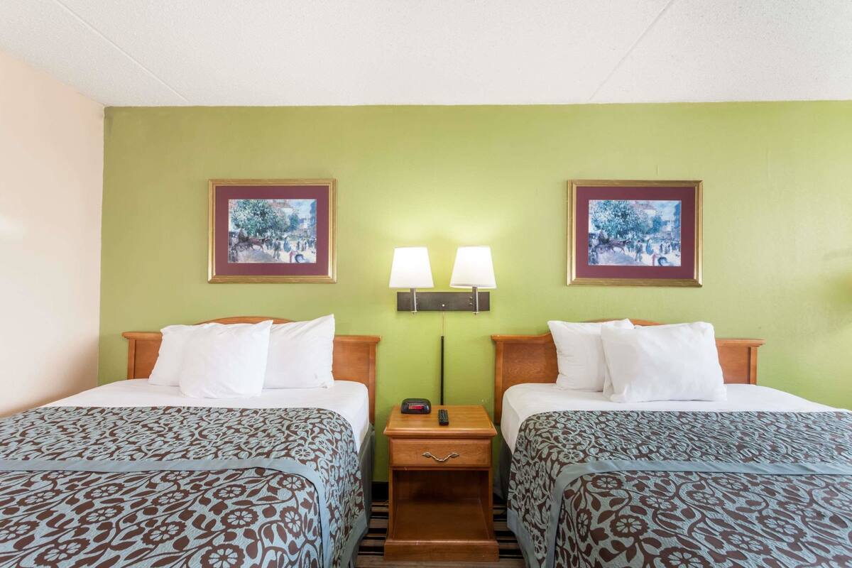 Une chambre d’hôtel avec deux lits, des murs verts et des tableaux encadrés au-dessus des lits.