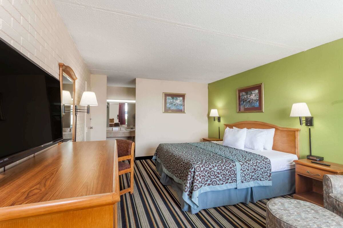 Une chambre d’hôtel avec un lit, un bureau, une télévision et deux lampes.